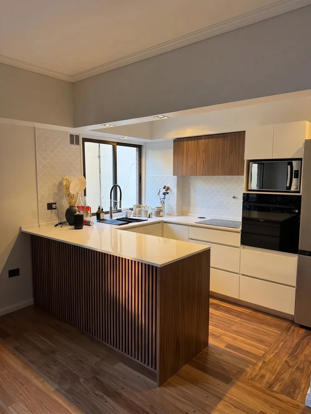 Diseño de cocina blanca con península revestida en listones y alacena de madera