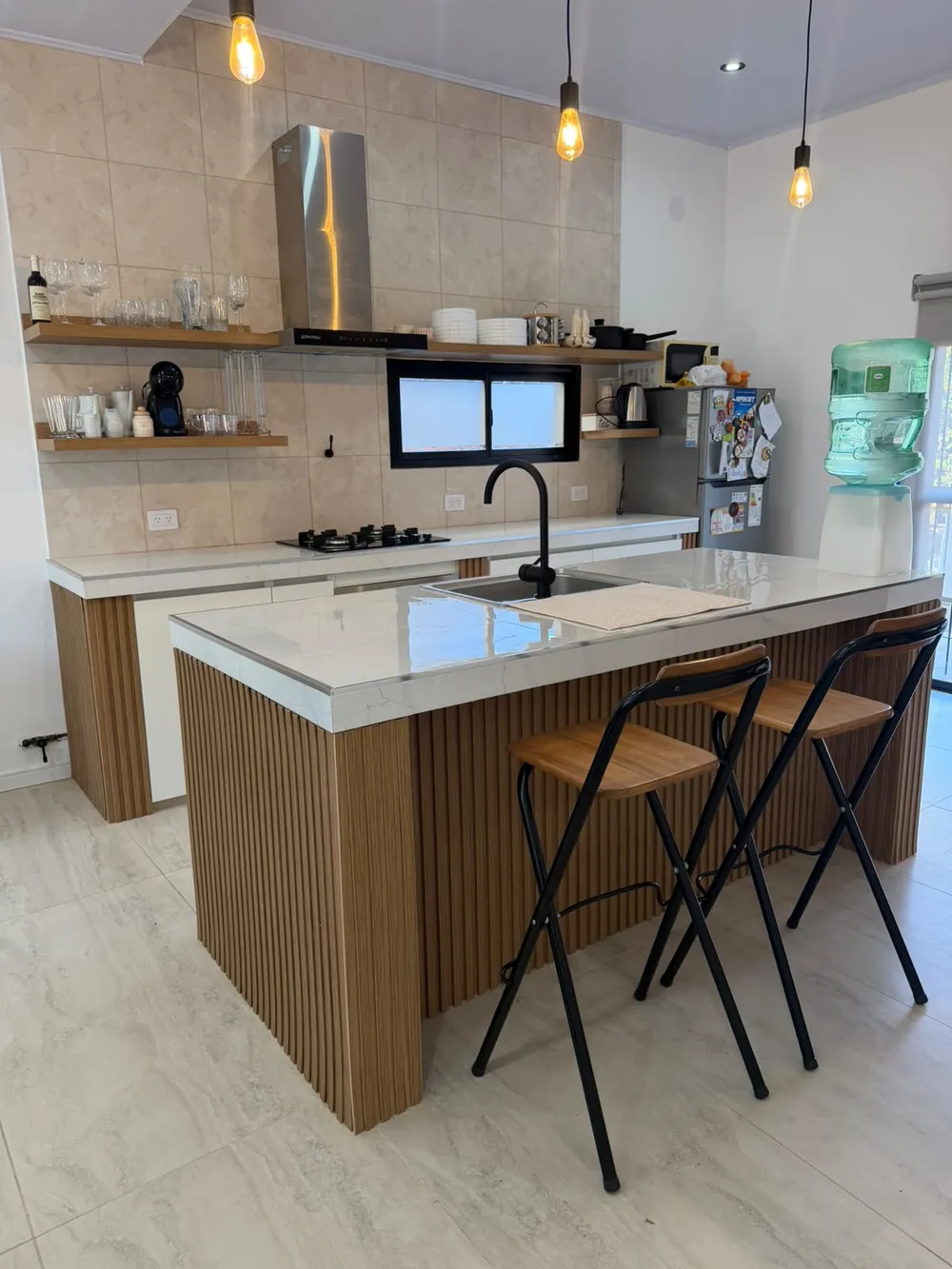 Cocina blanca con isla revestida en listones de madera y banquetas