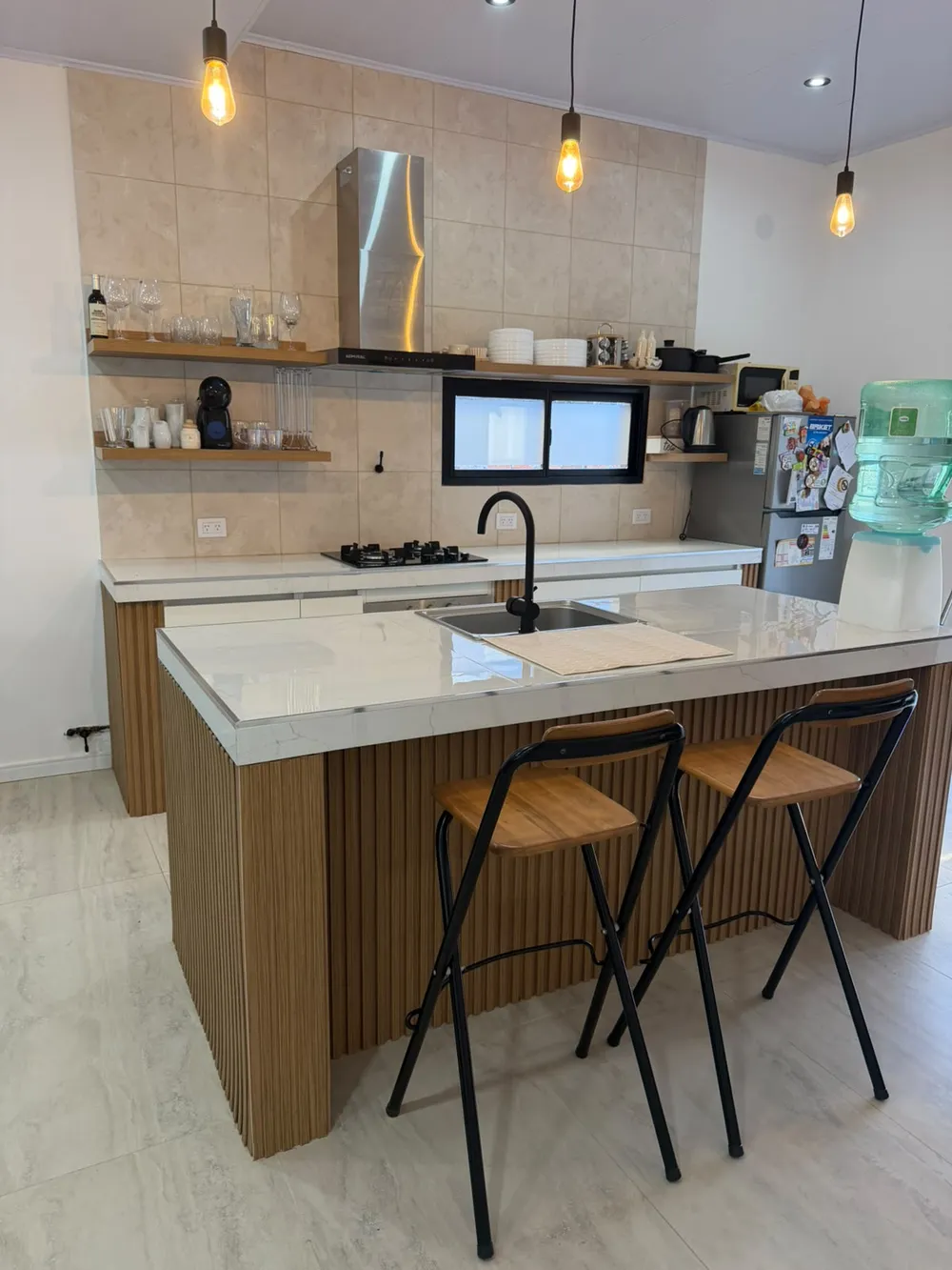 Cocina blanca con isla revestida en listones de madera y banquetas
